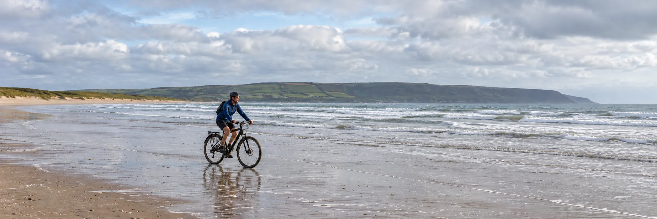 Cyclist riding along a beach shoreline in North Devon